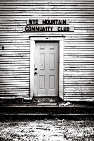 Black and white photo of the Wye Mountain Community Club building entrance with a weathered door and worn siding.