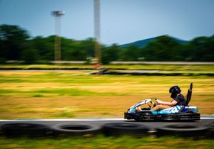 Person racing a blue go-kart at high speed on an outdoor track, with motion blur emphasizing the fast pace.