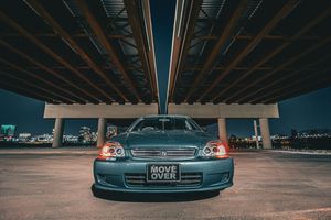 A lowered Honda Civic with a Move Over license plate posed under a highway overpass at night.
