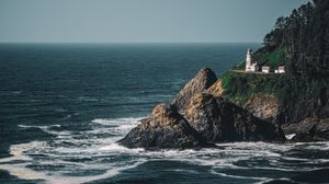 A white lighthouse perched on a rocky cliff overlooking the dramatic Pacific Ocean waves below.