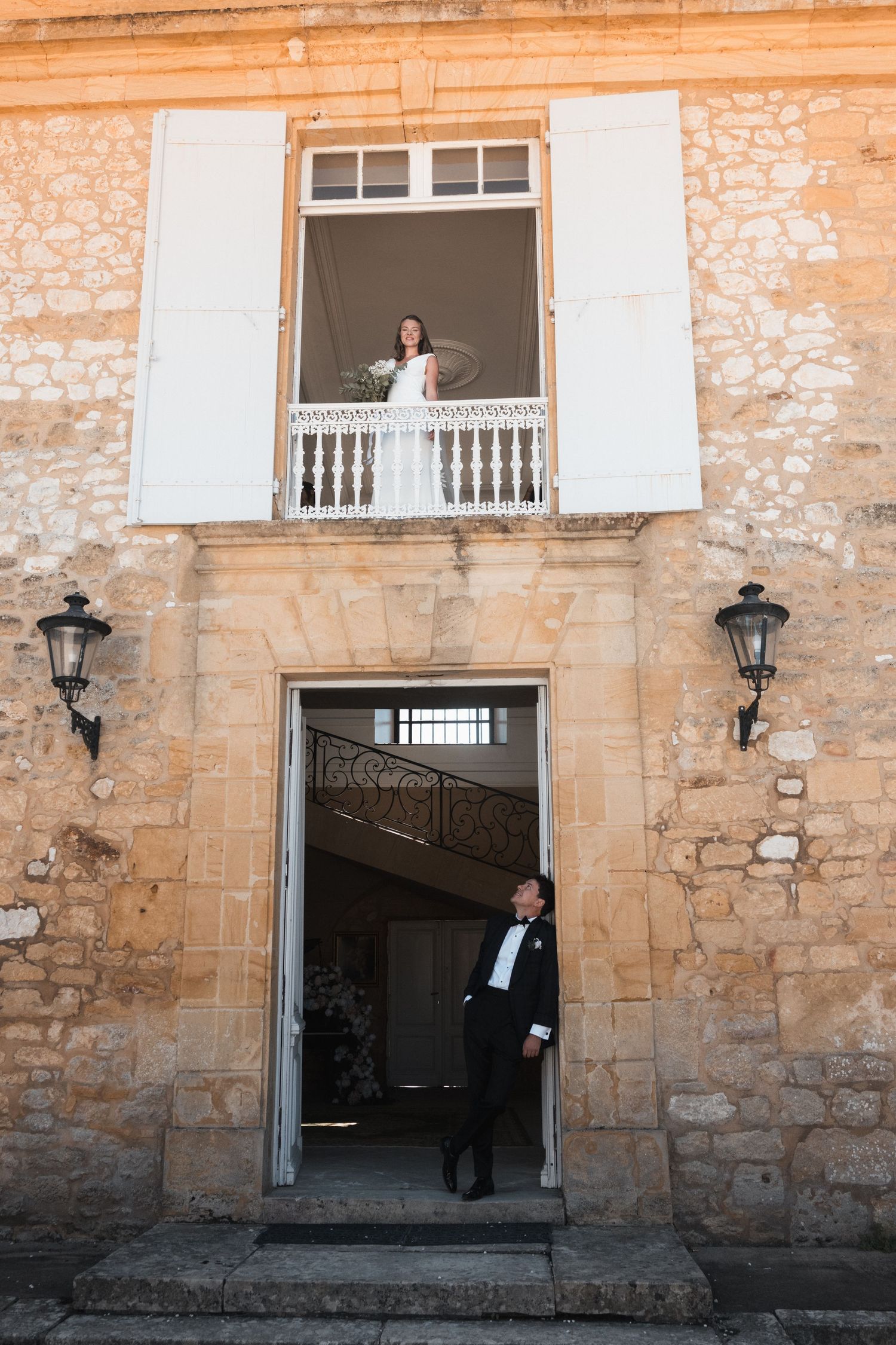 Beth on the château balcony with Matt standing in the doorway below.