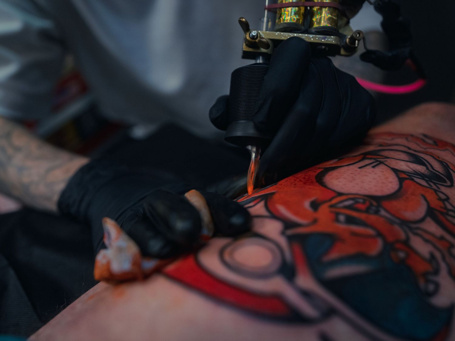 Karl Cooper's gloved hands work a tattoo machine into a bold red-and-black leg tattoo at Sacred Art Tattoo in Honolulu, Hawaii, ink pooling.