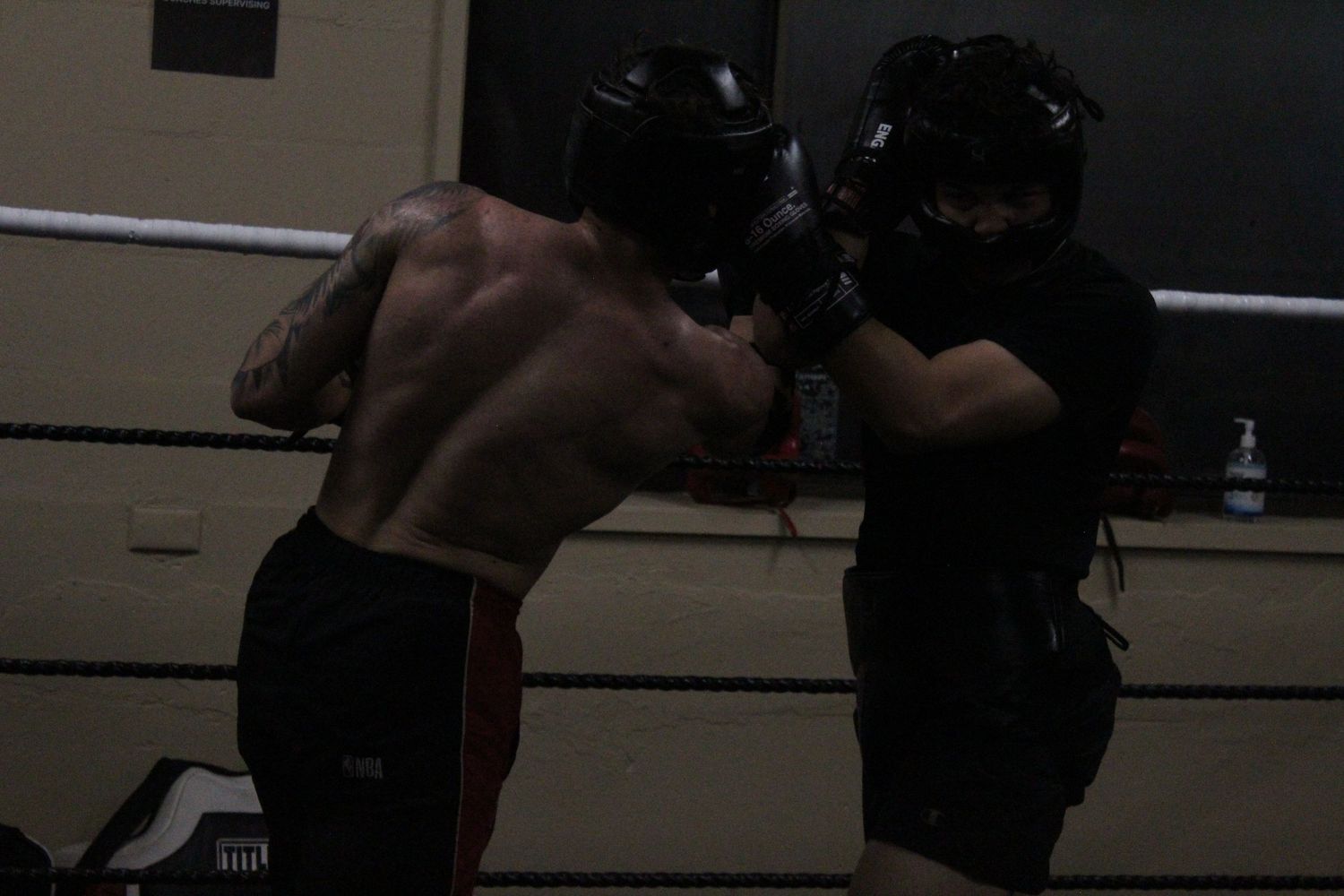 Two boxers sparring in a dark boxing ring wearing protective headgear.