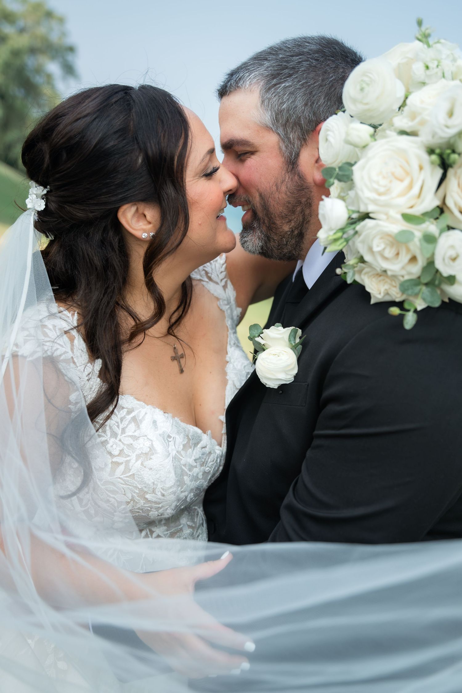 Newlywed couple walks down outdoor aisle at oceanfront wedding ceremony with white floral arch and lanterns.