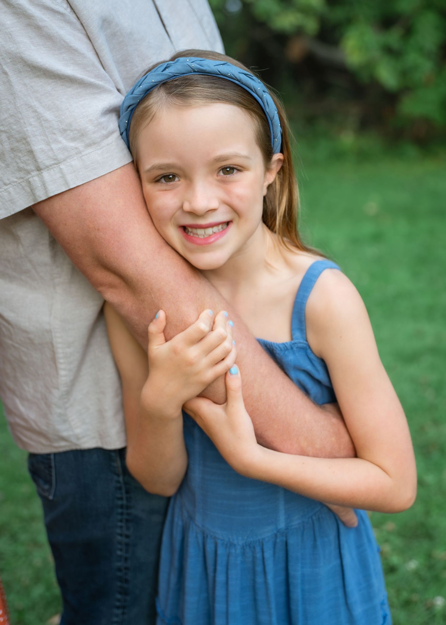 Two young girls in matching blue dresses and headbands share a sweet moment outdoors on green grass.