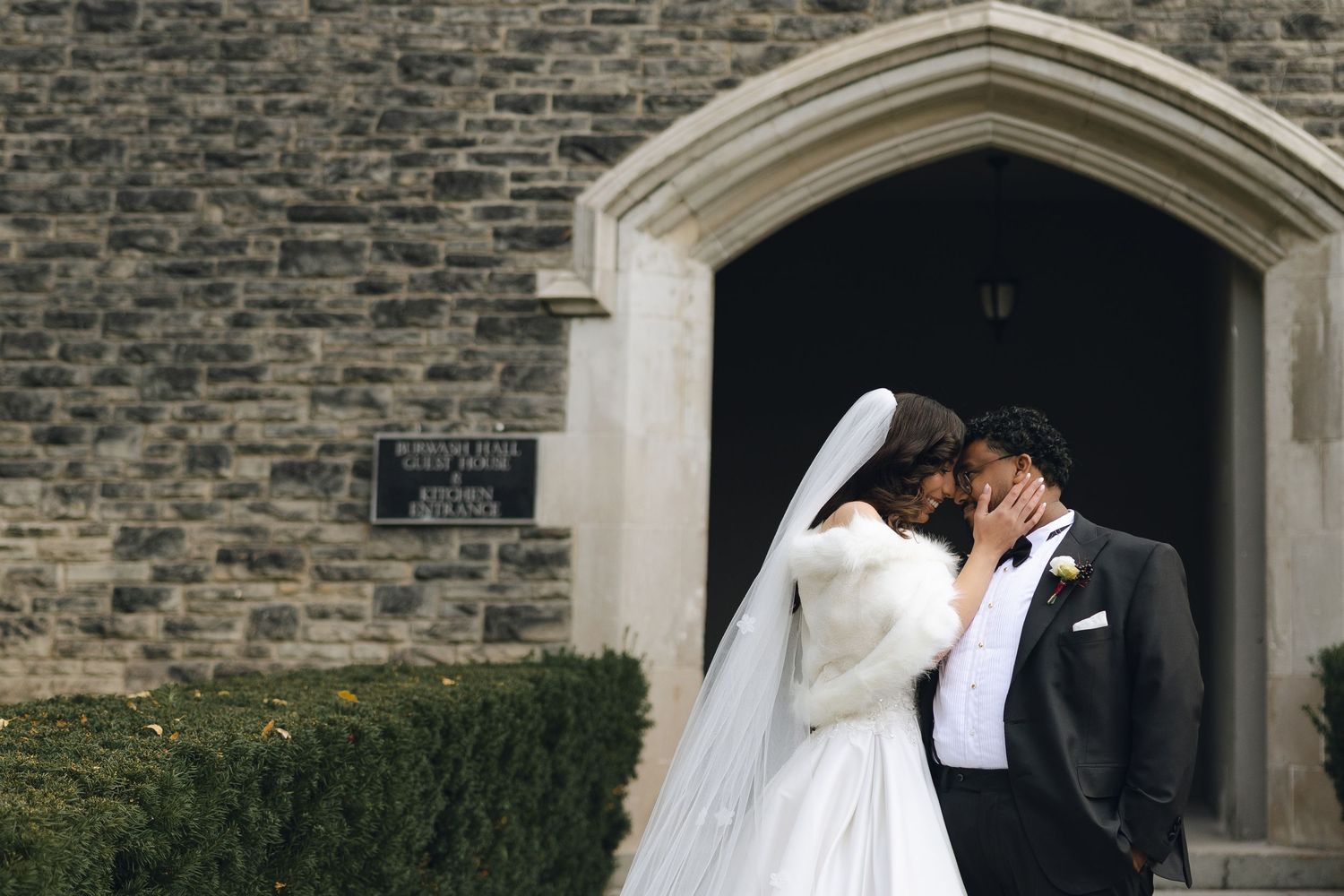 A bride and groom share a romantic kiss outside a stone church on their wedding day.