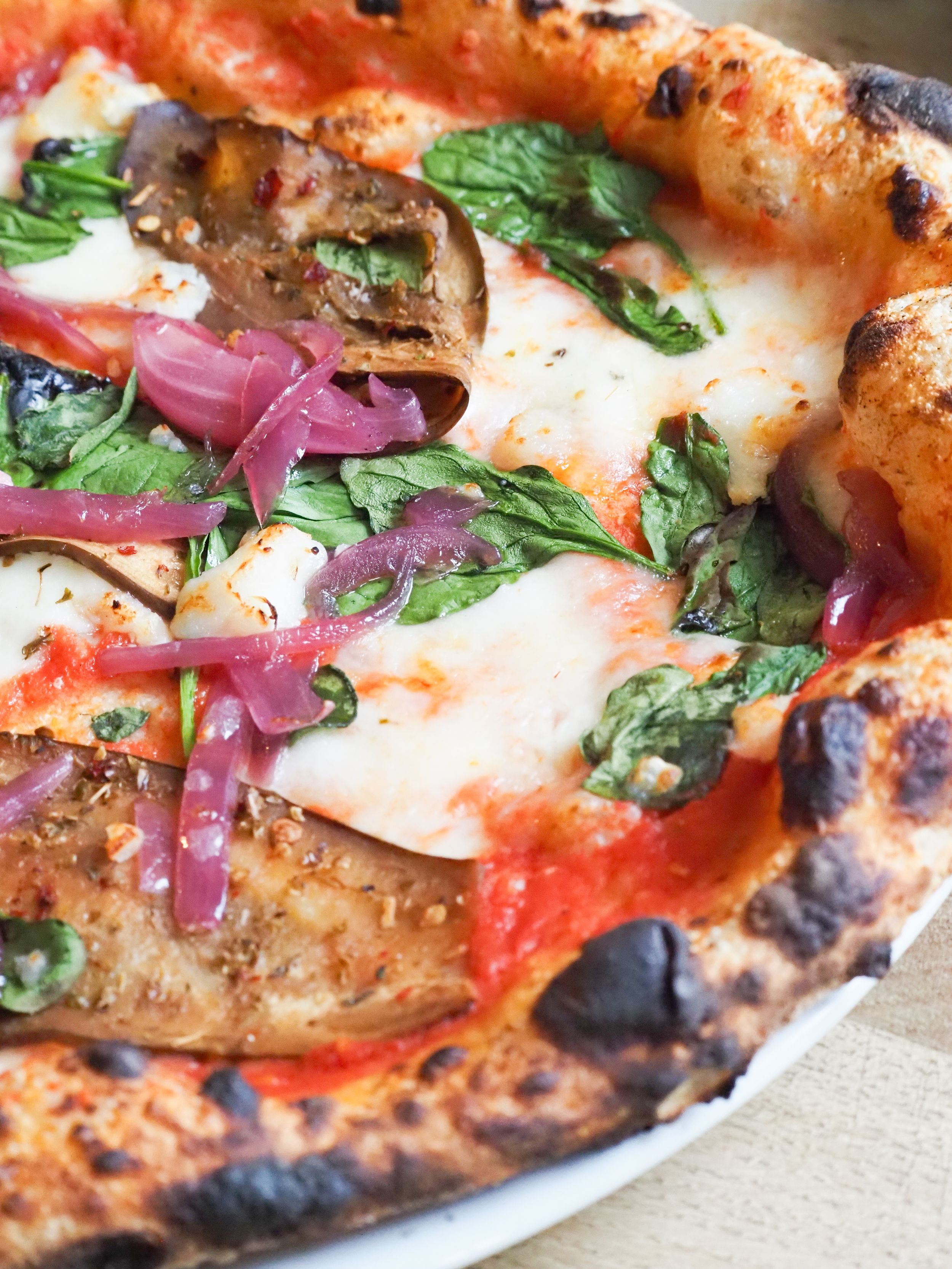 Close-up of wood-fired Neapolitan pizza with fresh mozzarella, red onions, mushrooms and basil on a charred crust.