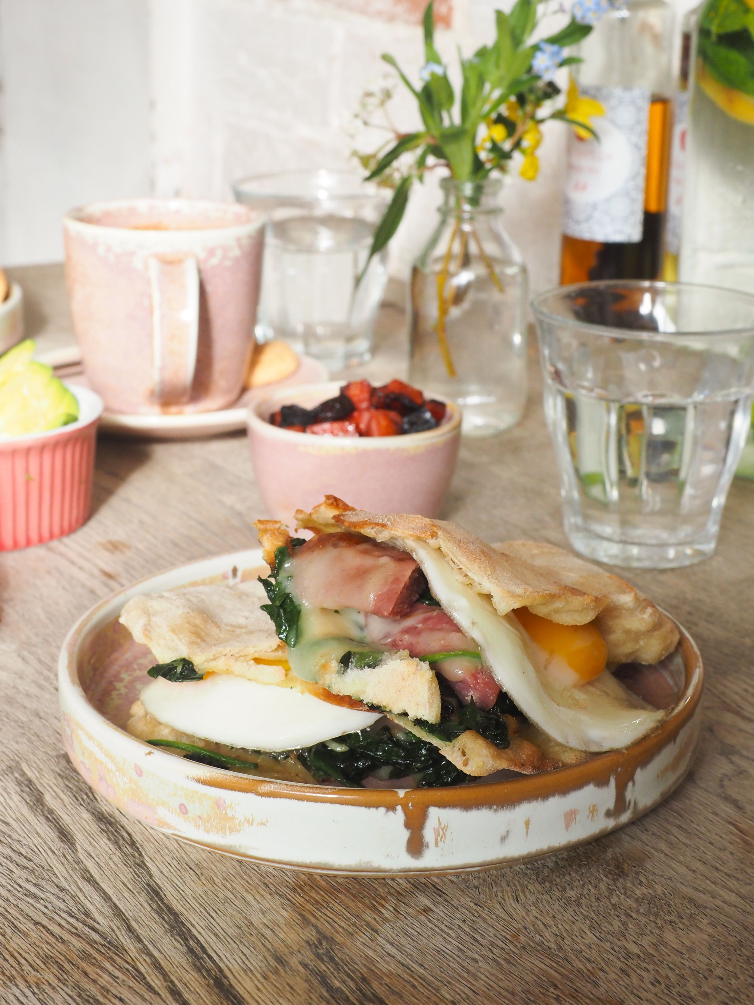 Brunch plate with eggs, ham and spinach on rustic bread served alongside coffee and berries on a wooden table.