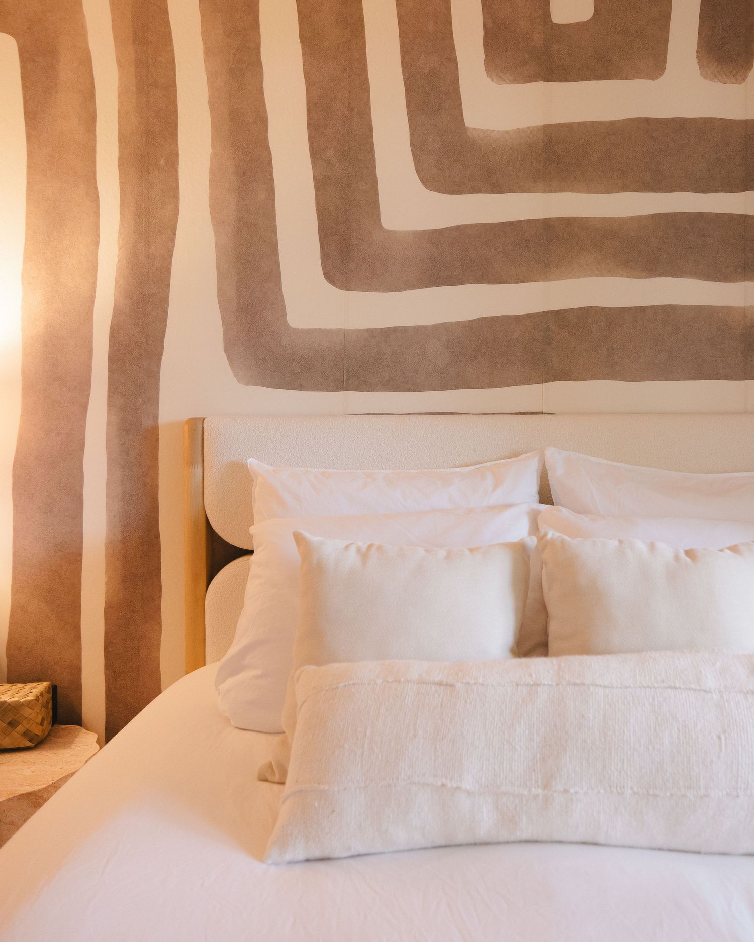 Cozy hotel bedroom with white pillows and linen bedding against a beige abstract striped mural wall.