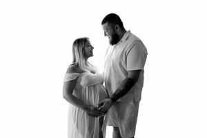 Black and white maternity photo of a couple holding the pregnant woman's baby bump in a studio.