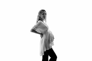 Black and white profile photo of a pregnant woman in a white top and black pants posing against a white background.