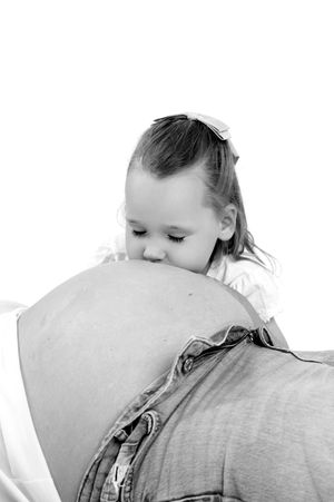 Young girl kissing pregnant mother's belly in black and white maternity photo.
