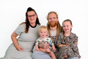 Family portrait of parents with two young children smiling together against a white background.