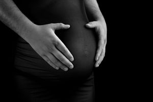 Black and white close-up of pregnant woman's belly with partner's hand gently resting on it.