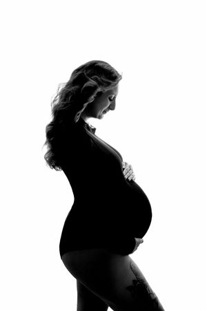 Black and white silhouette of a pregnant woman cradling her baby bump, profile view against white background.