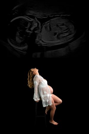 Pregnant woman in white lace robe sits on stool with ultrasound image overlay on black background.
