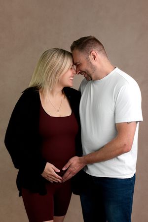 A couple sharing a tender forehead touch while cradling a pregnant belly during a maternity photo session.