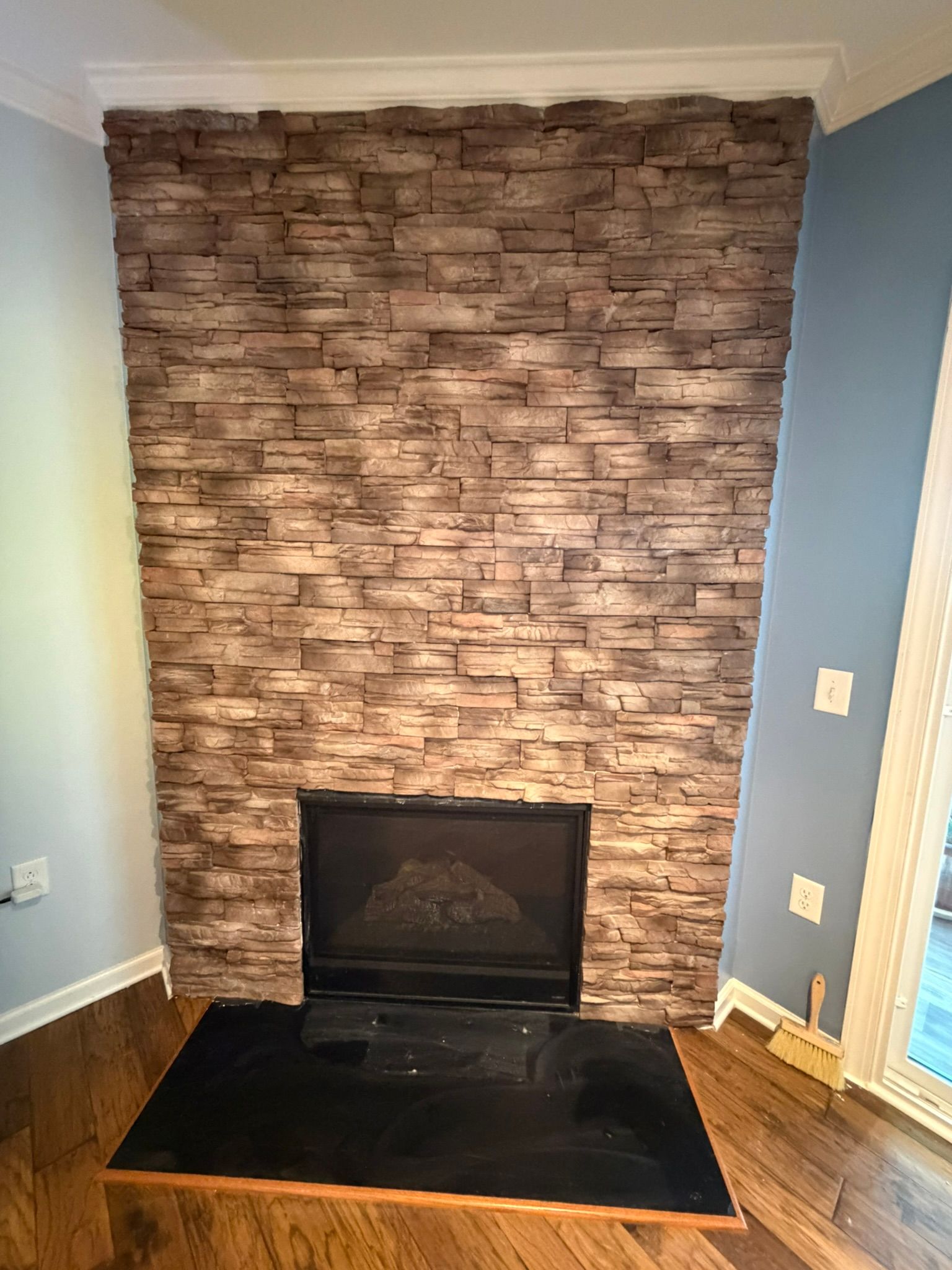 Floor-to-ceiling stacked stone veneer fireplace surround with rustic brown tones on hardwood floor interior.