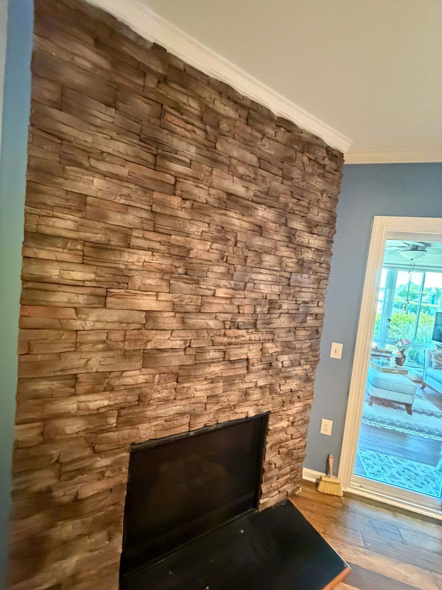 Tall stacked ledger stone fireplace accent wall with warm brown tones and crown molding in living room.