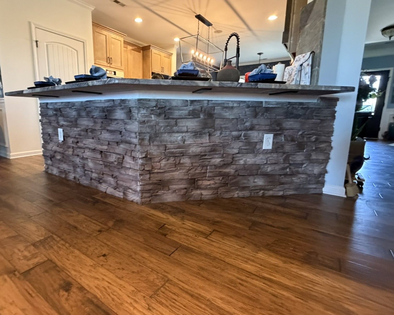 Modern kitchen island featuring stacked stone veneer siding with dark countertop and hardwood flooring.