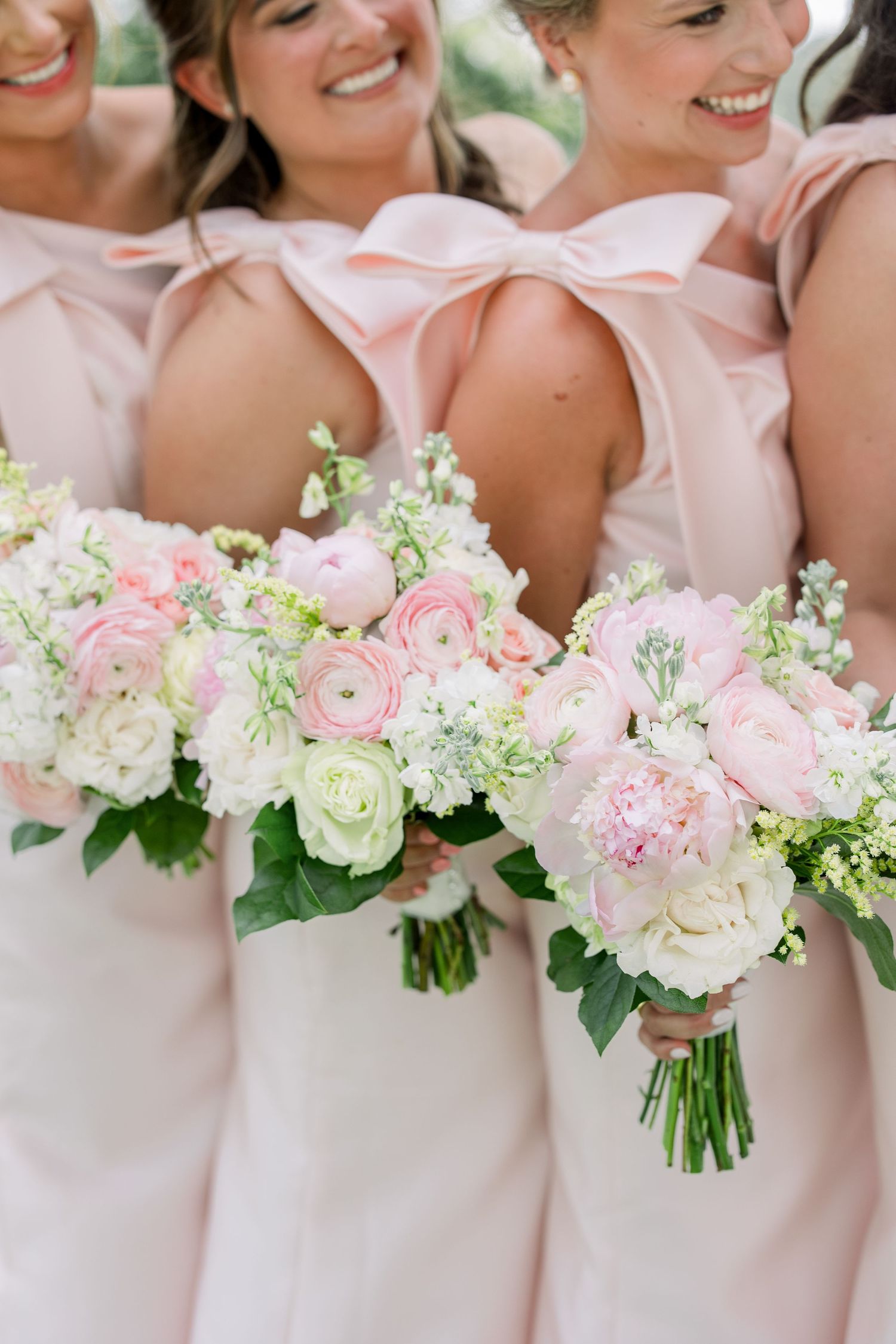 Bridesmaids in blush pink gowns with bow backs holding white and pink ranunculus wedding bouquets at lake martin alabama.