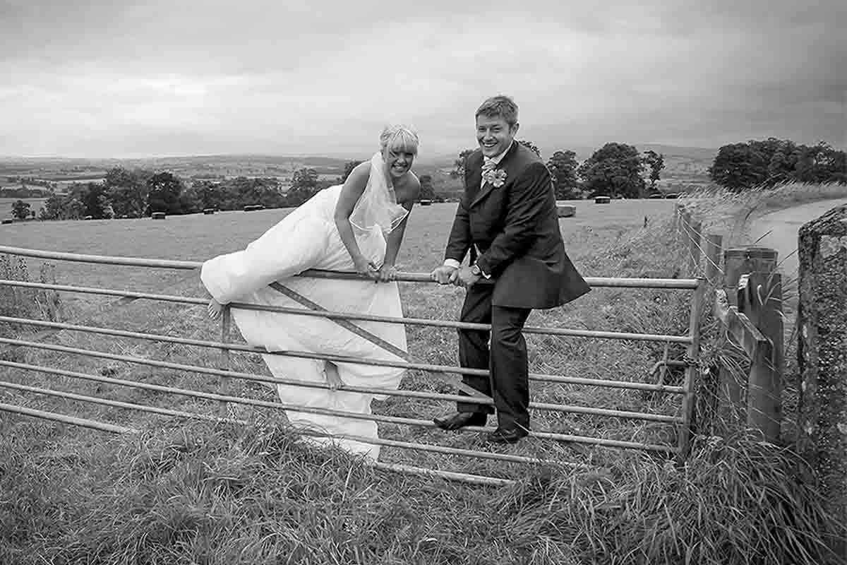 Bride and groom climbing a farm gate at Roundthorn Country House, Penrith, on their wedding day.