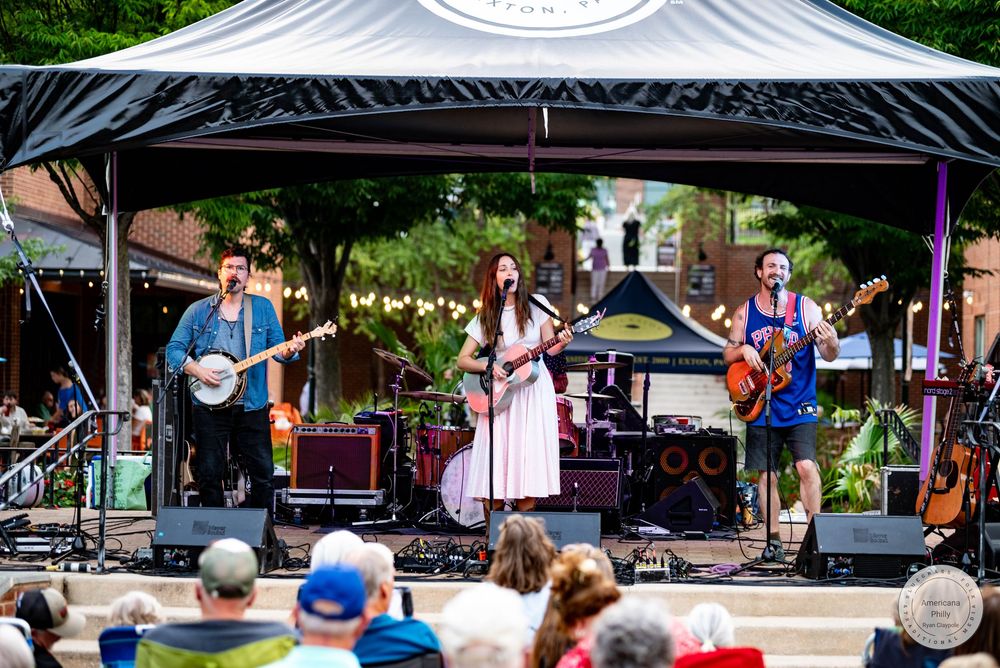 Live outdoor band performance with four musicians on stage at a sunny festival event.