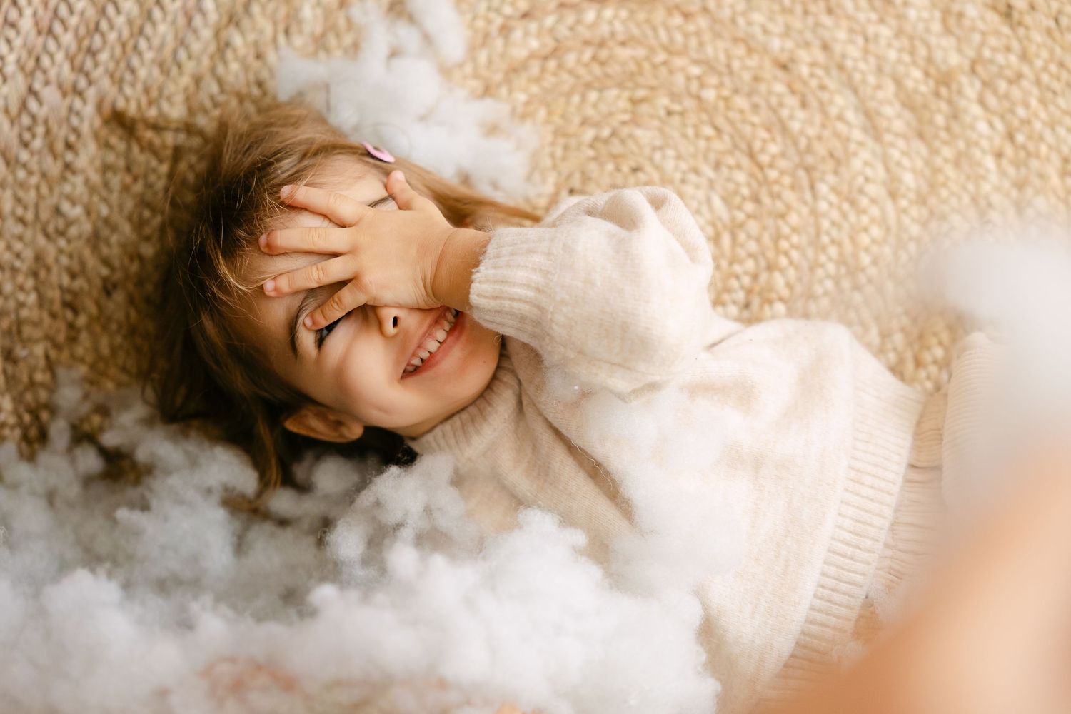 Child laying on cream colored bedding with twinkling lights and sheer curtains in background.