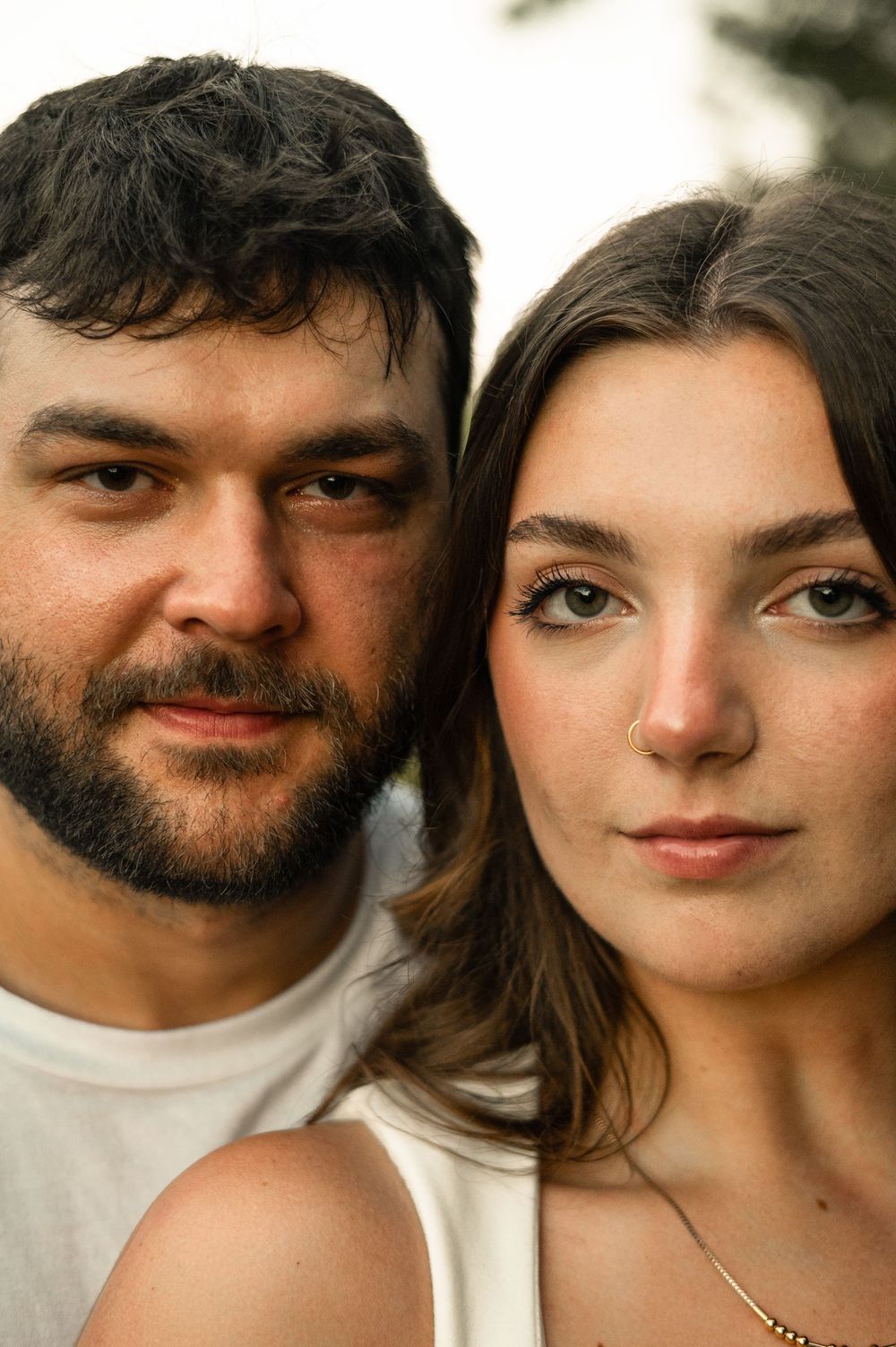 Close-up portrait of a young couple in white tops posing together, man with dark beard and woman with brown hair.