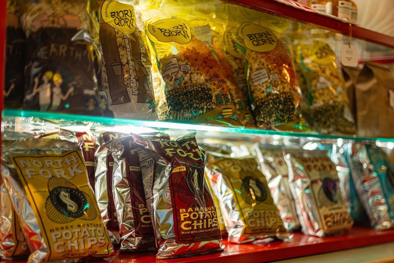 Colorful bags of potato chips displayed on illuminated red shelves in a snack shop.