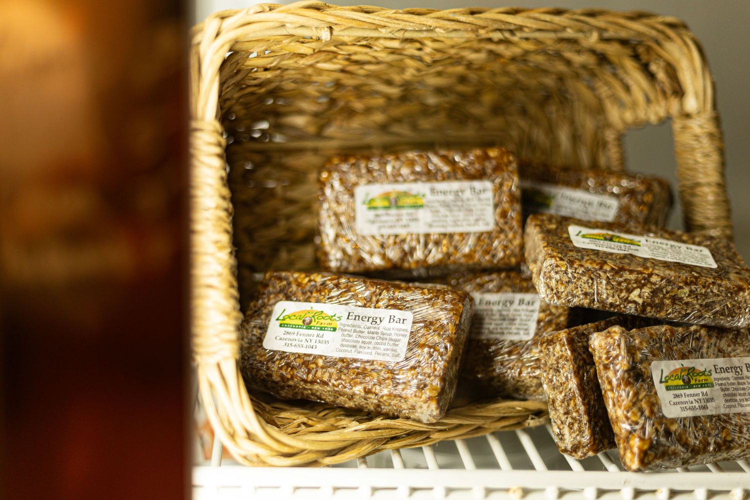 Homemade granola energy bars displayed in a wicker basket on a white shelf in a bakery or health food store.