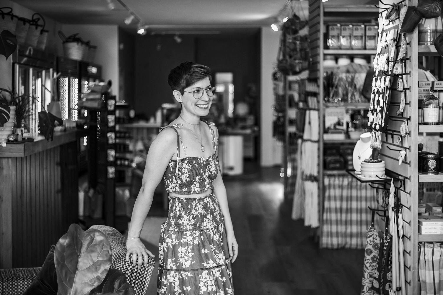 Woman in floral dress smiling in a charming boutique shop, black and white photo.