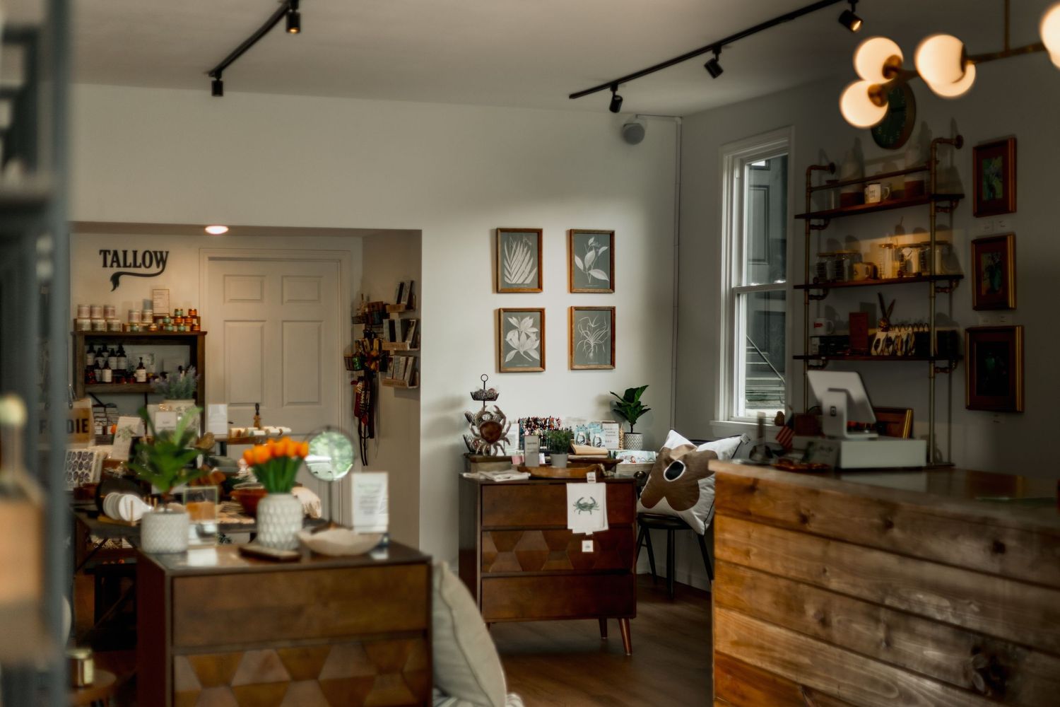 Cozy boutique shop interior with rustic wooden furniture, orange tulips, framed art, and warm track lighting.
