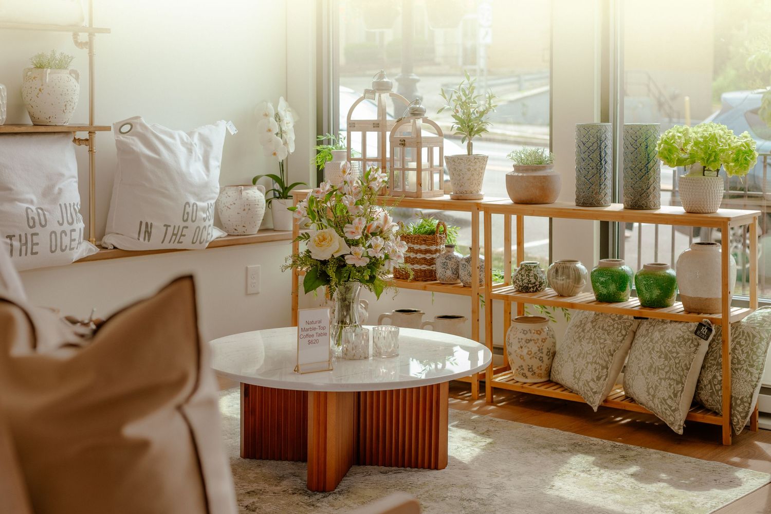 Bright boho living room with bamboo shelves, potted plants, floral arrangement, and a round marble coffee table in warm sunlight.