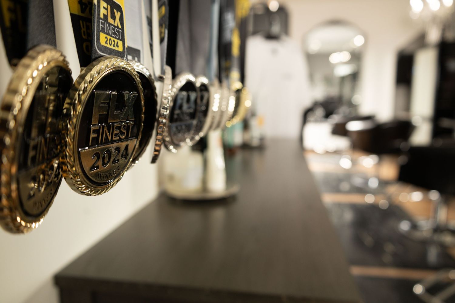 Close-up of FLY Finest 2024 award medals displayed on a shelf in a modern hair salon.