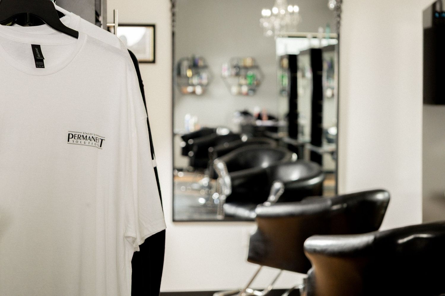 White salon cape hanging in a modern hair salon with black chairs and a large mirror in the background.