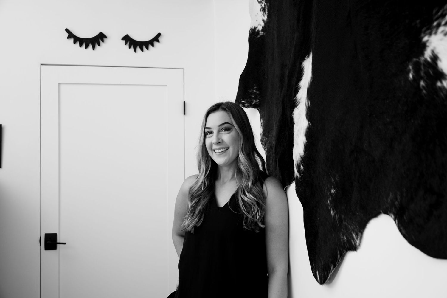 Smiling woman with long blonde hair in black top, standing in modern black and white decorated room.