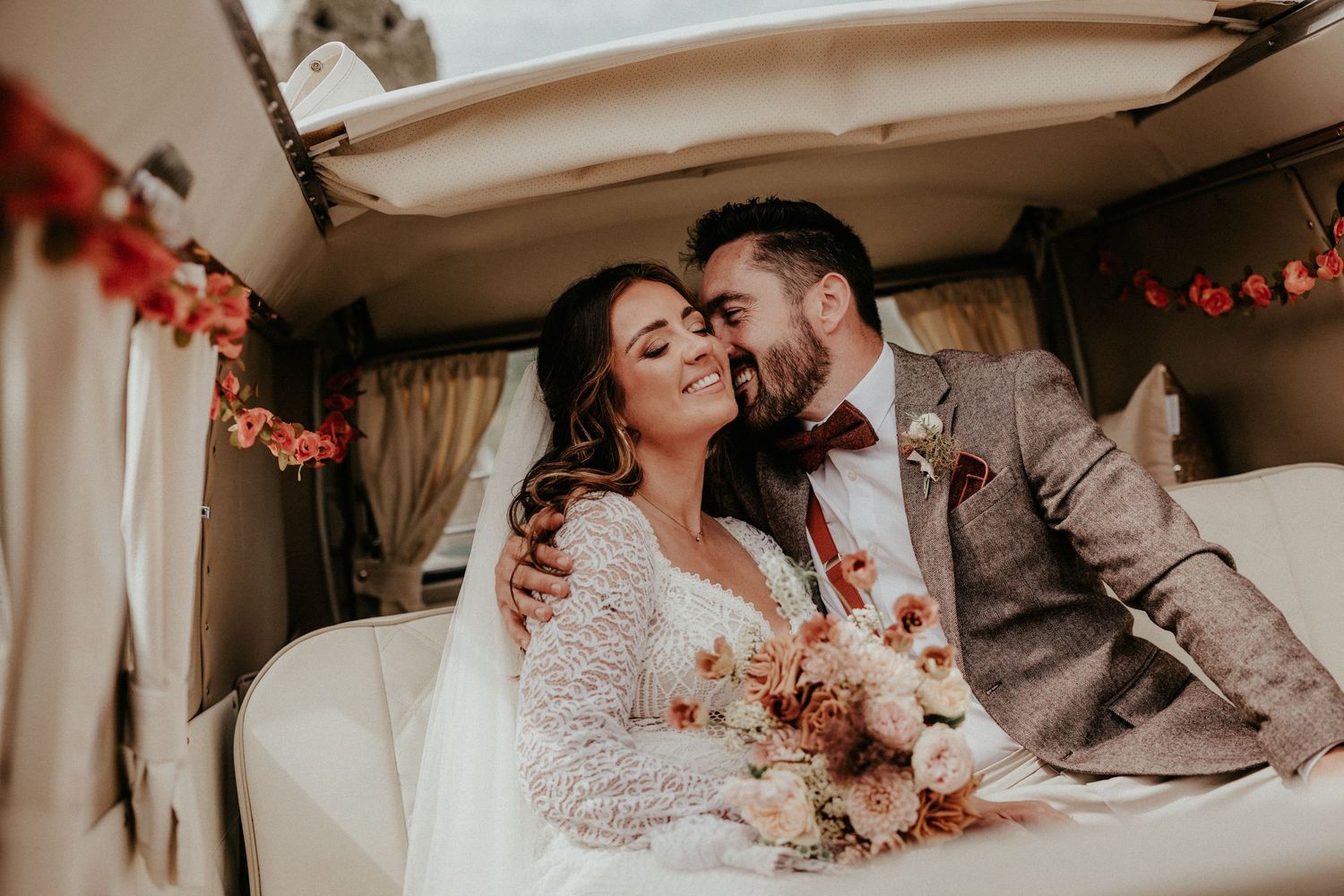 Bride and groom share a romantic moment inside a vintage van, bride holding a boho bouquet.