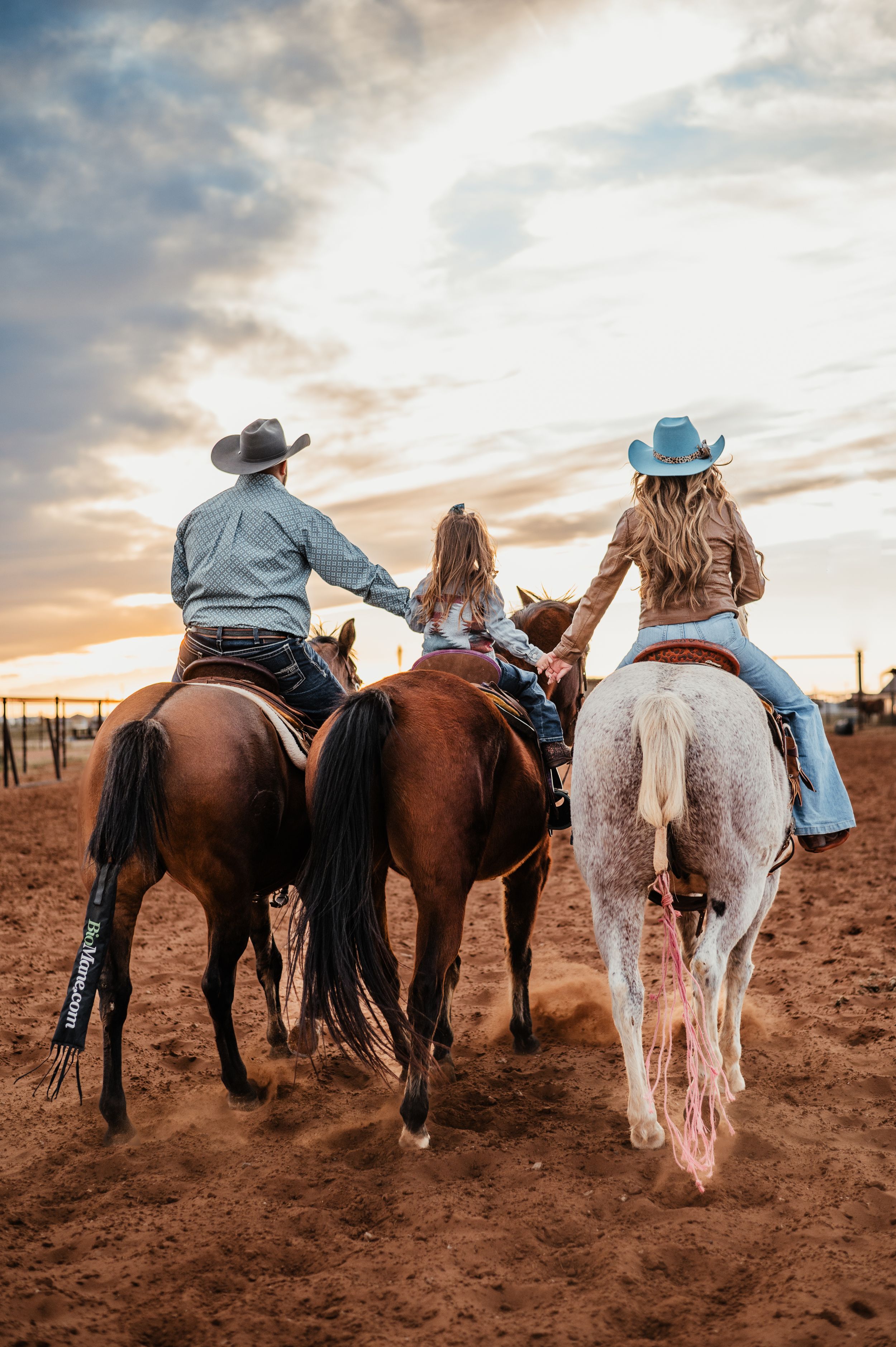 Three people riding horses together at sunset on a desert trail.