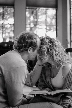 Black and white image of intimate reading moment by window.