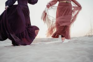 Close-up of flowing dresses moving in wind on sandy beach.