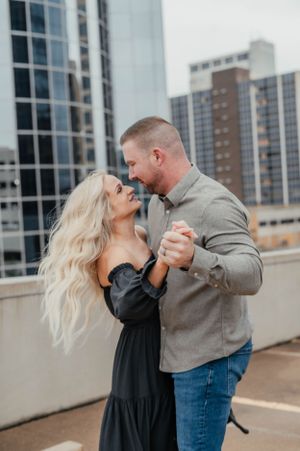 A romantic couple dancing and embracing on a rooftop with city buildings in the background.