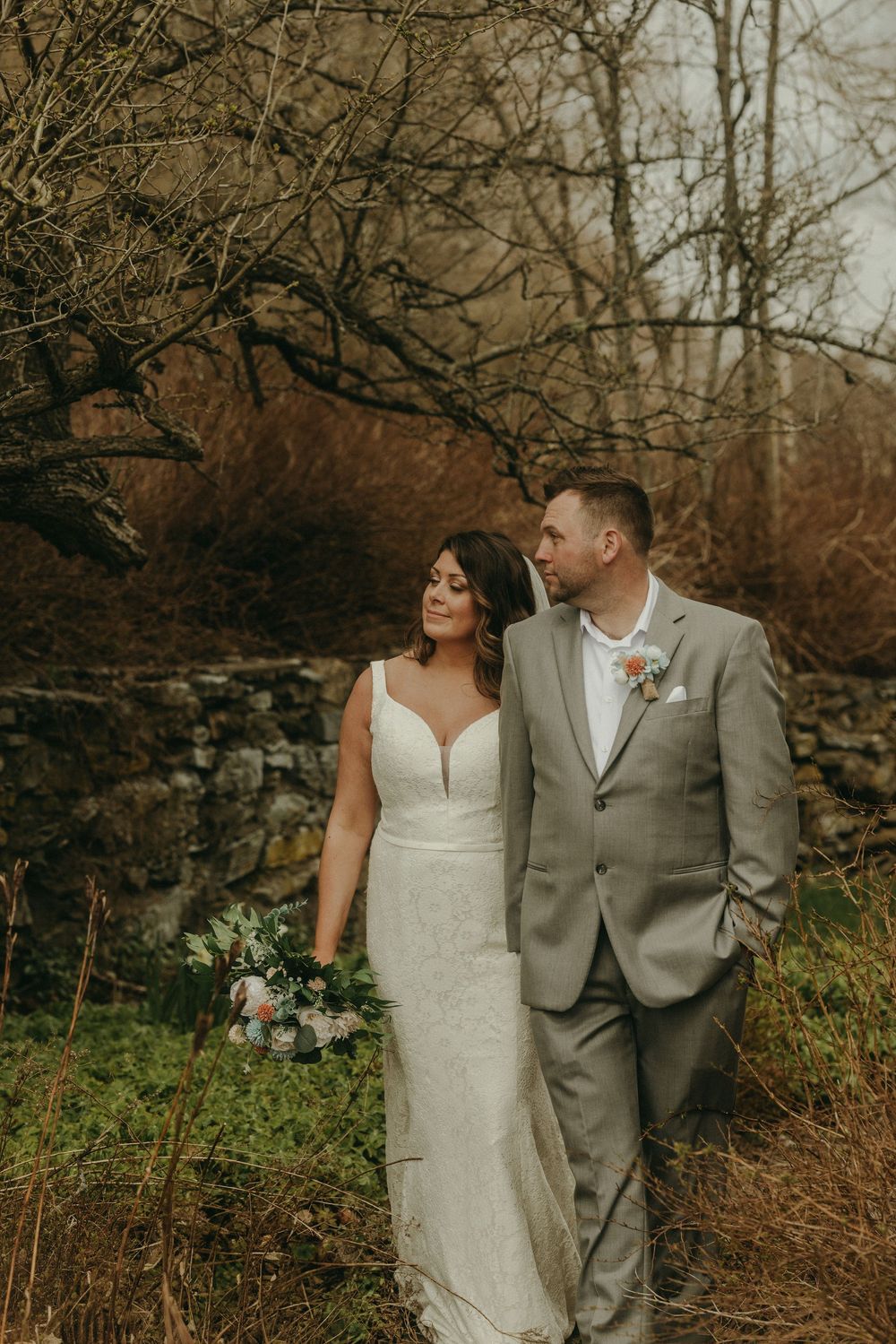 Newlyweds share an intimate moment against a rustic stone wall backdrop on their wedding day.
