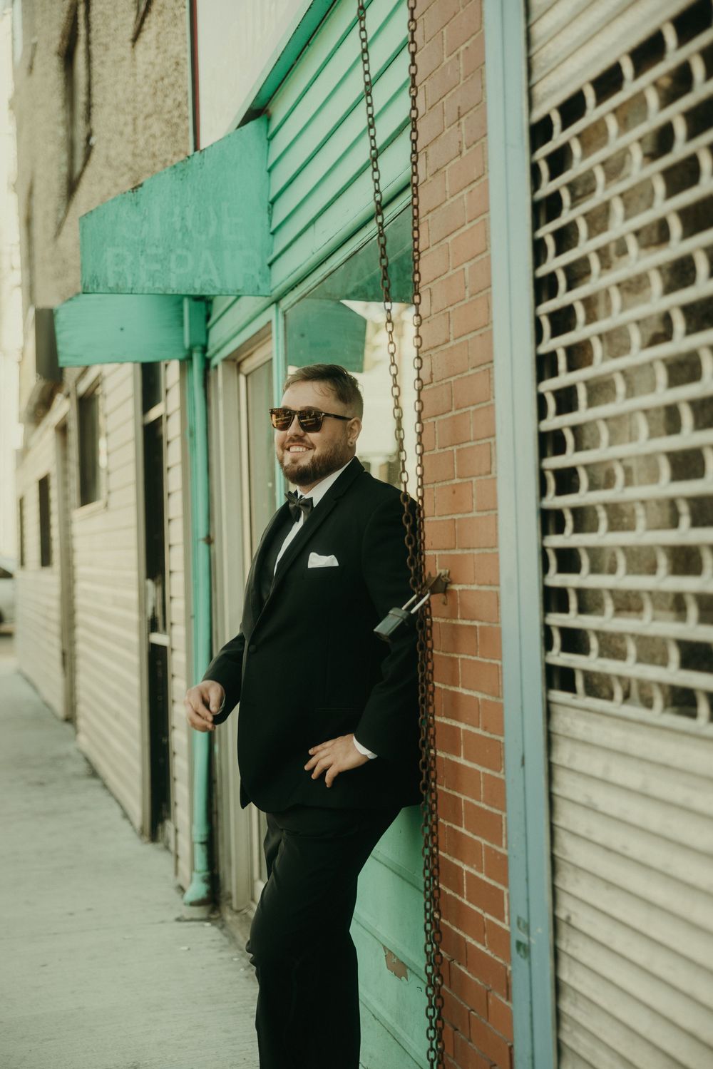Formal wedding party member poses against brick wall with mint green trim.