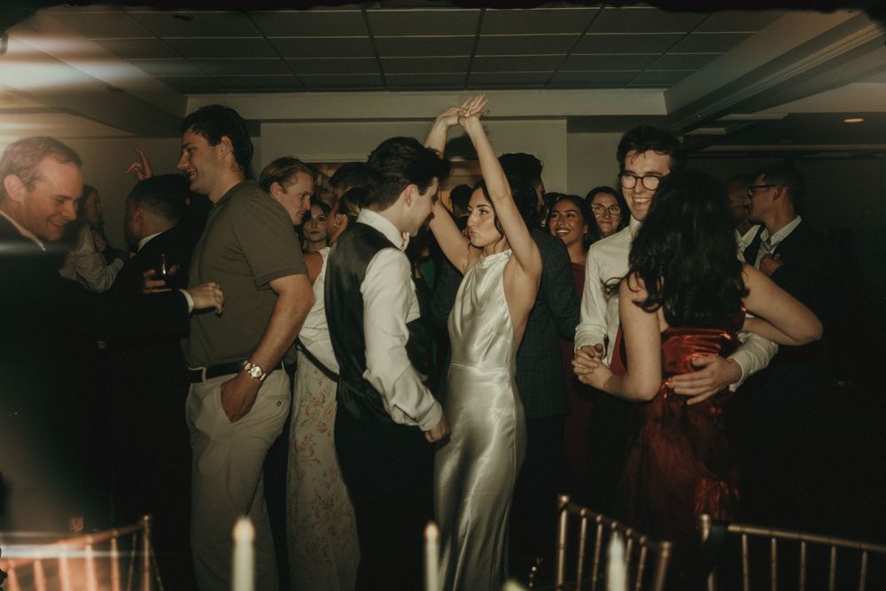 Wedding guests celebrate on the dance floor at an indoor reception.