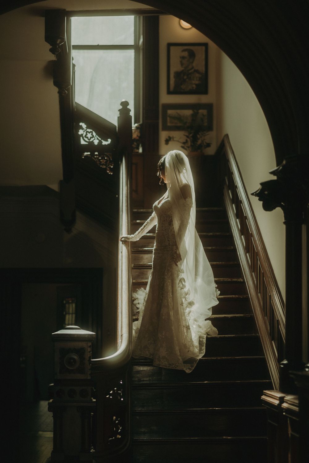 Ethereal bridal silhouette descending historic wooden staircase in dramatic lighting.