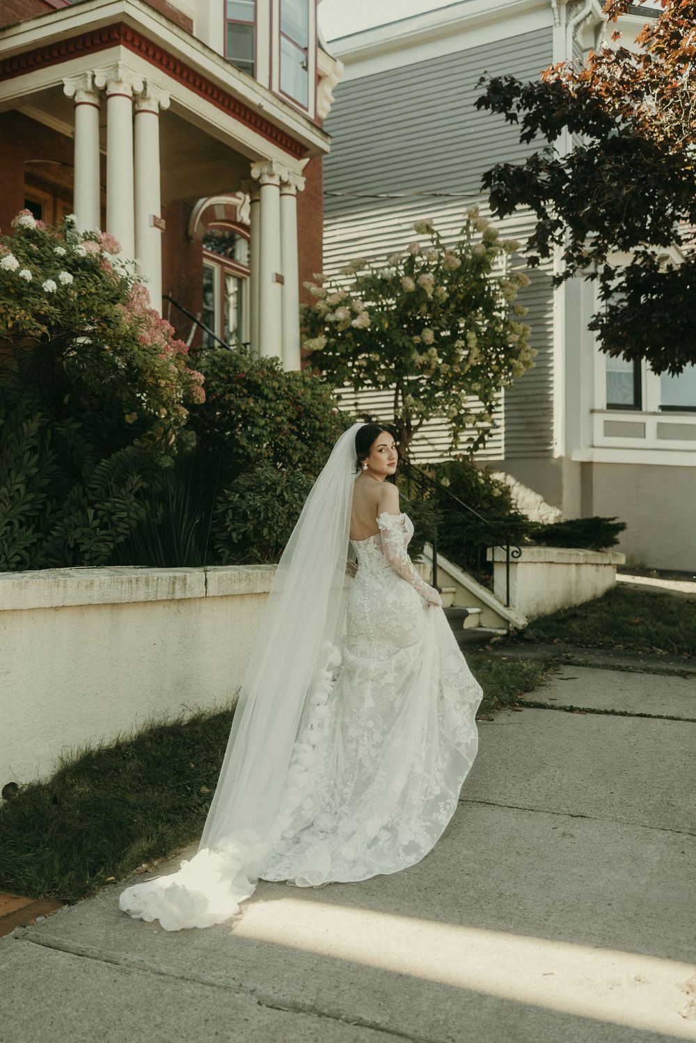 Wedding dress train flows beautifully across concrete steps of historic white building.