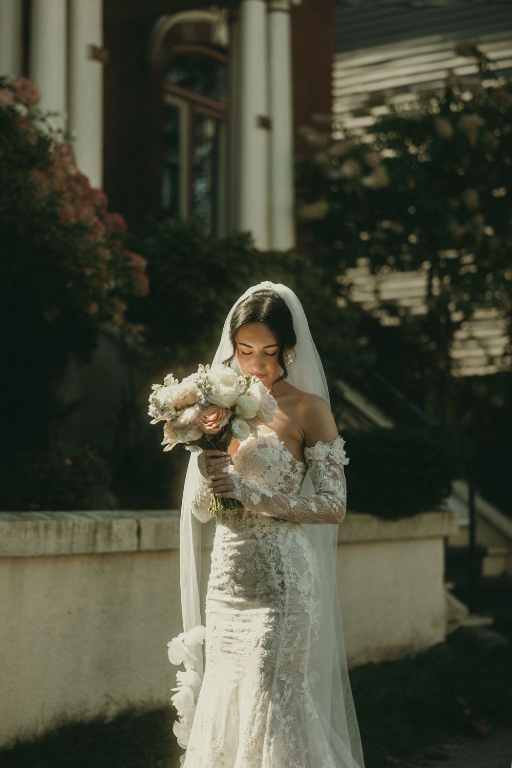 Delicate lace wedding gown and bouquet captured in soft natural light outside historic building.