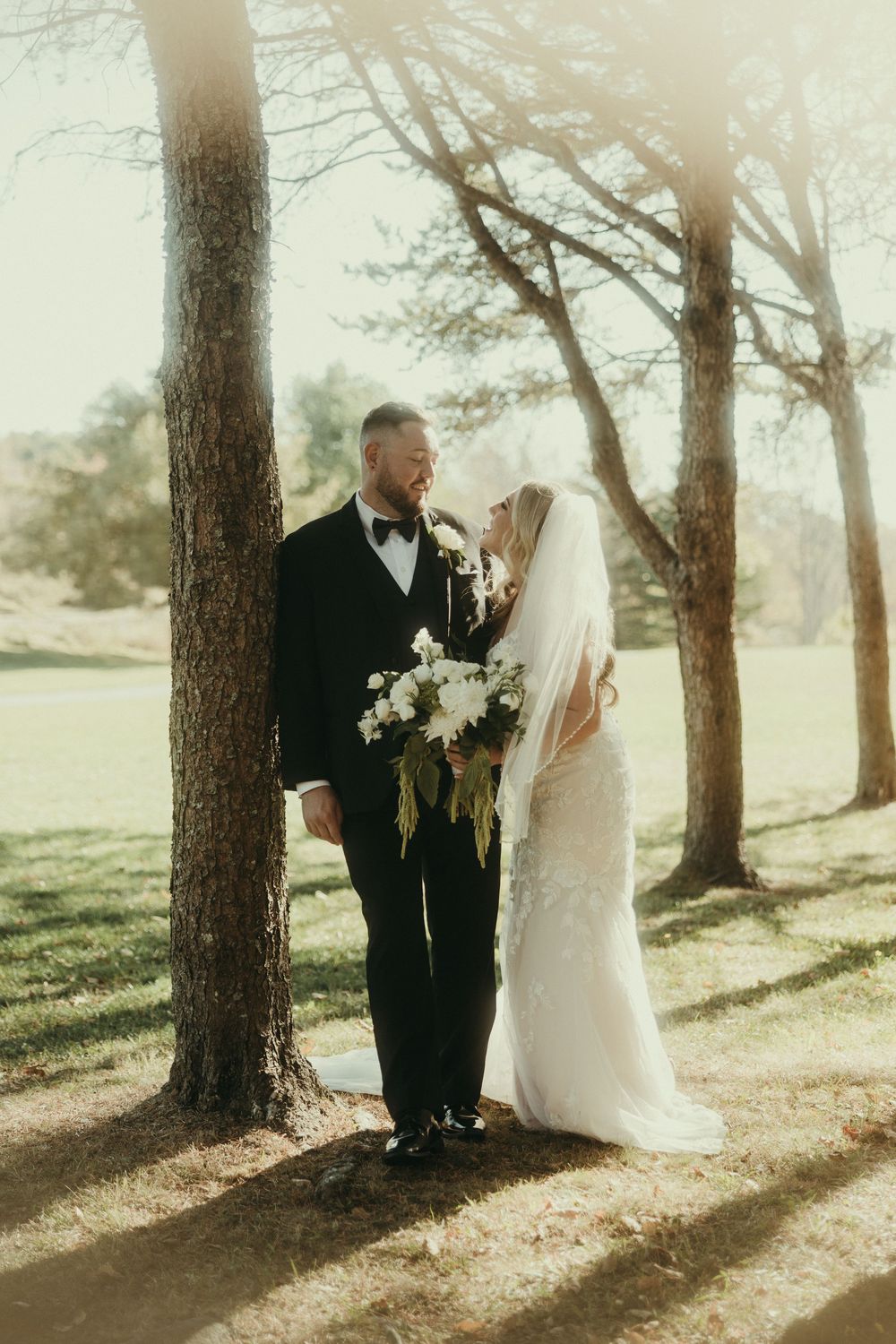 Sunlit wedding photos among tall pine trees creating dramatic shadows.