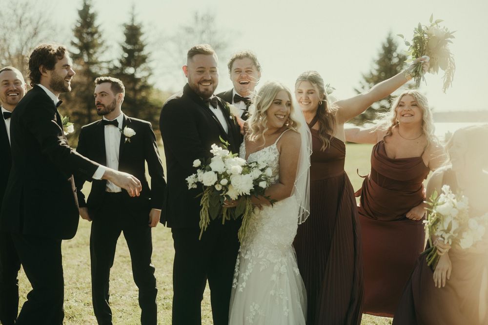 Wedding party celebrating outdoors with formal attire and burgundy accents.